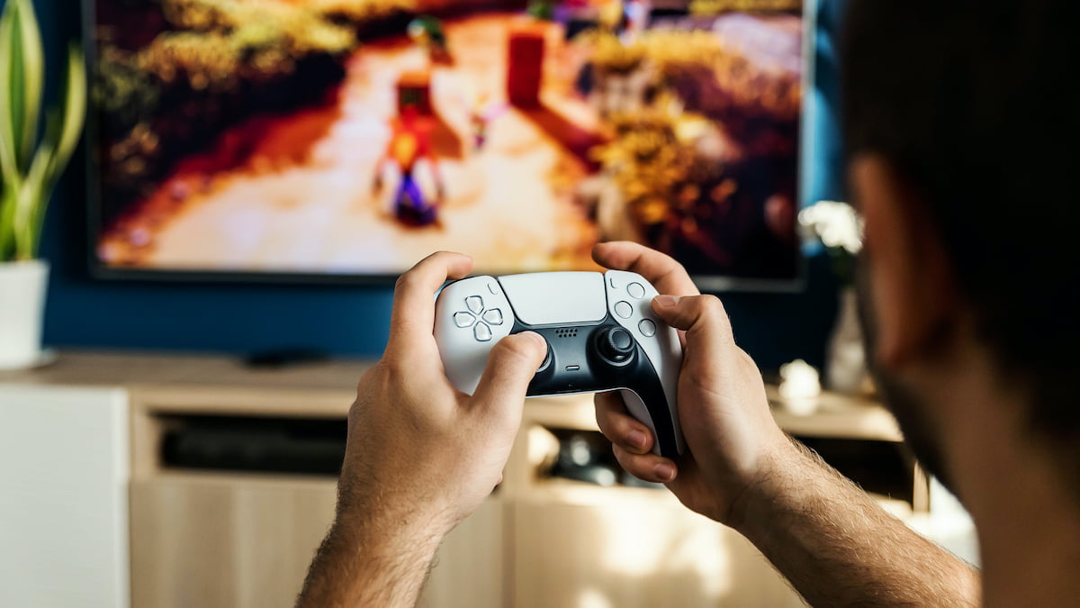 Male gaming using the Dualsense controller with PS5 and TV at the background