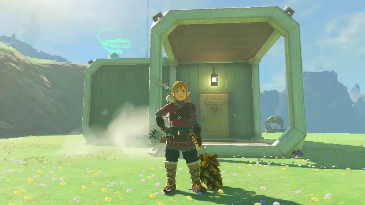 Link standing in front of a built home in Zelda Tears of the Kingdom. Grass is present along with mountains in the background.