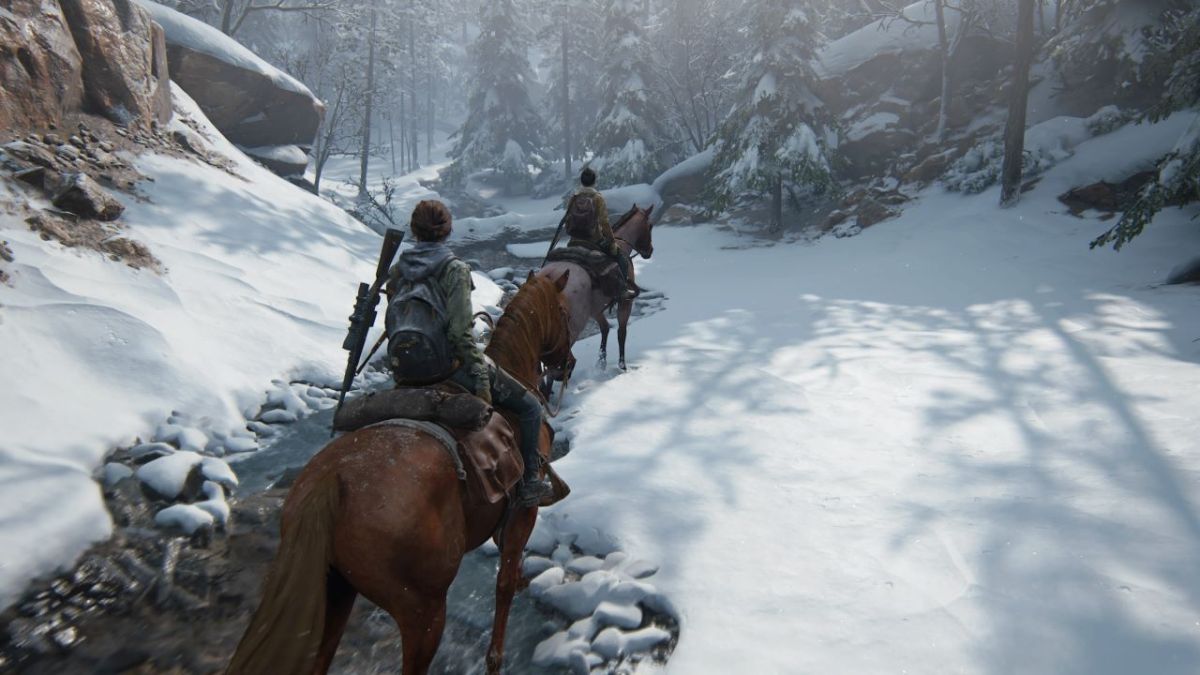 Image of Ellie and Dina in The Last of Us Part II riding horses through a snowy landscape with a stream in the middle.