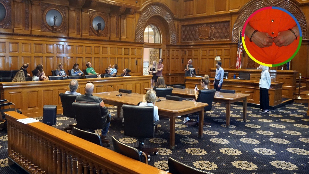 A courtroom with people seated inside and an inset image of a person in an orange jumpsuit wearing handcuffs.