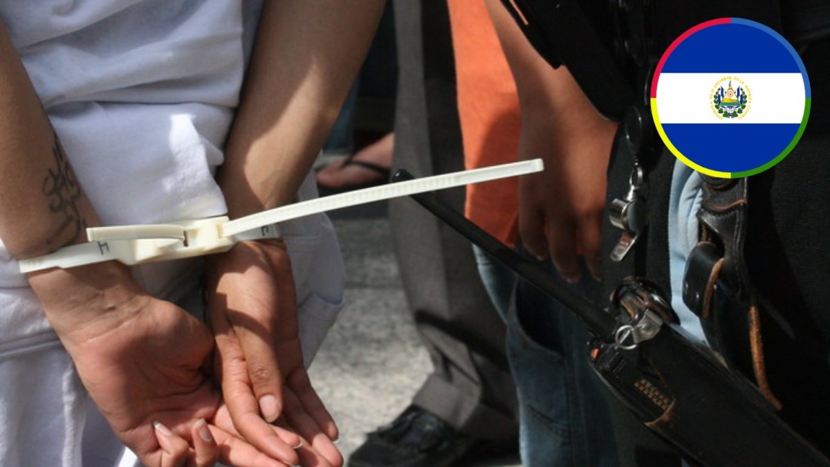 Person’s hands secured behind their back with plastic restraints, with an inset graphic of the El Salvador flag.