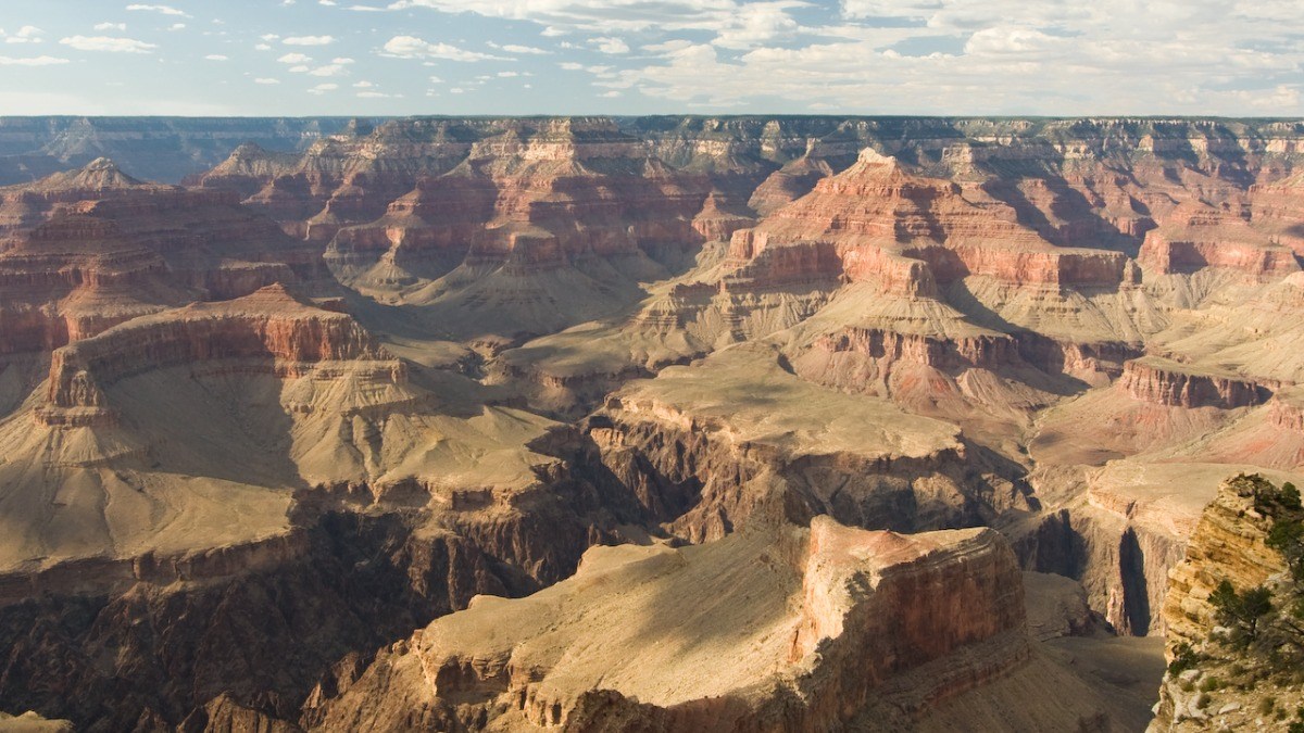 Wide view of the Grand Canyon showing layered red rock formations and deep valleys under a partly cloudy sky.