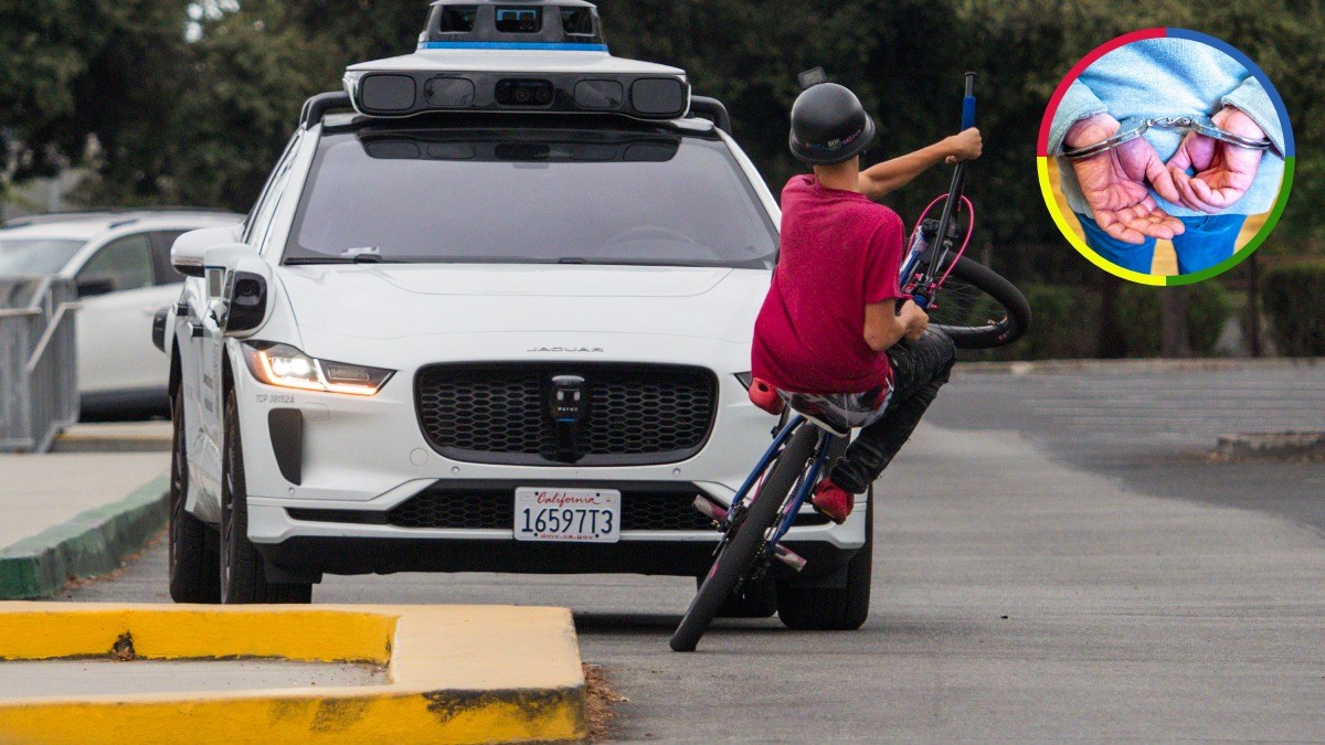 A cyclist performing a wheelie in front of a Waymo self-driving vehicle, with an inset image of hands in handcuffs.